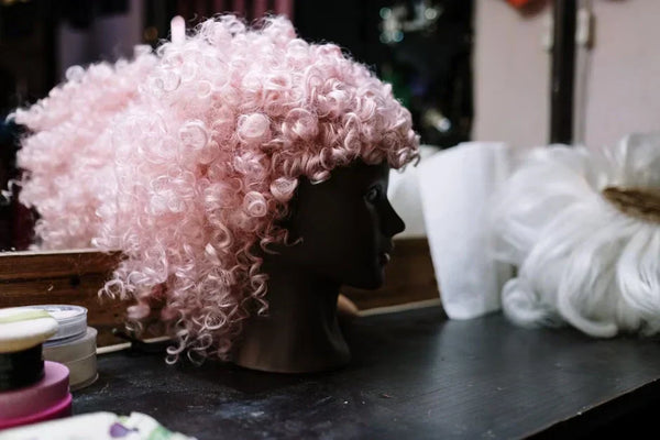 A curly pink wig placed on a mannequin head in an indoor dressing room setting