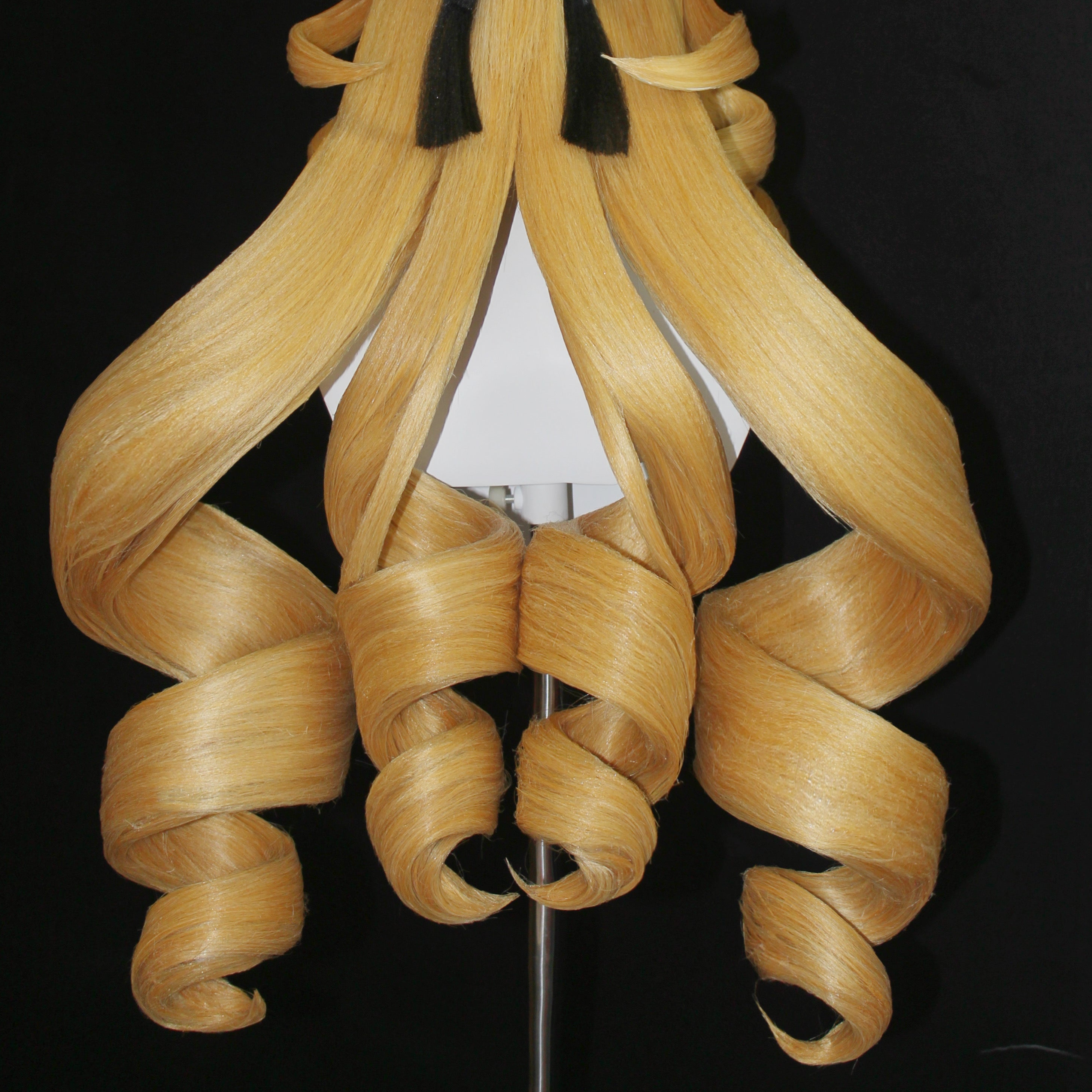 An extreme close-up detail of the Genshin Impact Navia cosplay wig by Koollia, showcasing the perfectly symmetrical, hollow blonde drill curls styled over a black background.